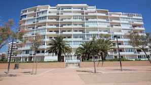 A multi-story hotel with balconies, palm trees, and a clear blue sky. - Modern Apartment with Panoramic Sea View & Terrace, by the Beach – Costa Brava (Roses)