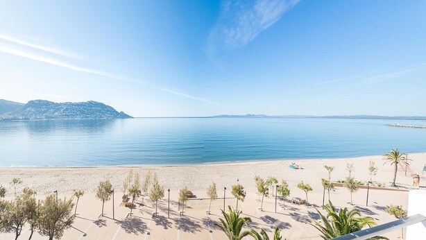A beach view with a clear sky, calm sea, and a distant mountain range. - Modern Apartment with Panoramic Sea View & Terrace, by the Beach – Costa Brava (Roses)