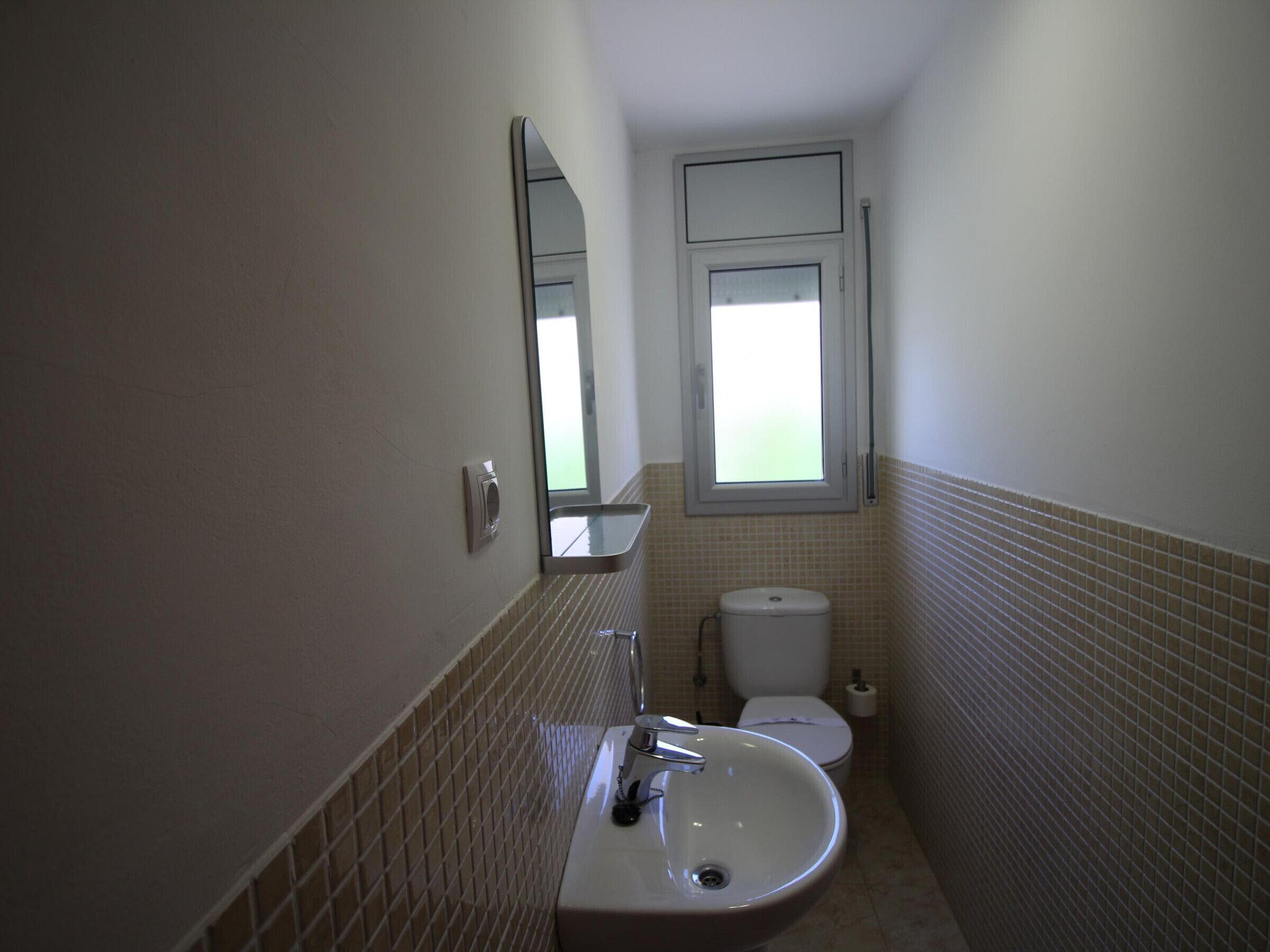 A narrow bathroom with a white sink, a mirror, and a toilet.