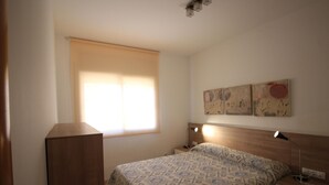 Une chambre à coucher comprenant un lit, des tables de chevet, une fenêtre avec des stores et des œuvres d’art murales.