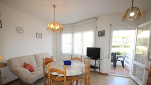 Uma sala de jantar com mesa e cadeiras, uma televisão sobre um móvel e um sofá.