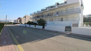 Edifício residencial com vários andares, varandas, calçada pavimentada e céu claro.