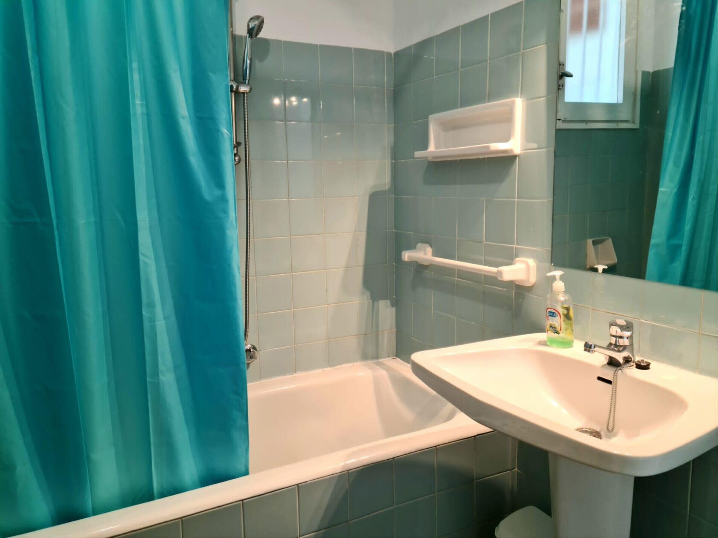 A bathroom with a bathtub, a sink, a showerhead, and a mirror.