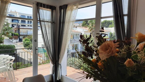 Un balcon avec une table et des chaises, un vase de fleurs et une vue sur le quartier.