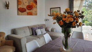 Un salon avec un canapé beige, une table sur laquelle est posé un vase de fleurs et un tableau accroché au mur.