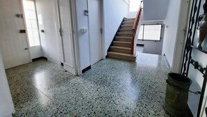 Un hall d’entrée spacieux avec un escalier menant à l’étage supérieur, des murs blancs et un sol à motifs.