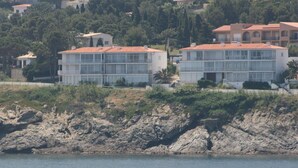 A coastal building with a red-tiled roof, large windows, and a rocky shoreline in the foreground. - Apartment with Terrace 300m from Beach, Parking Included (Llançà)