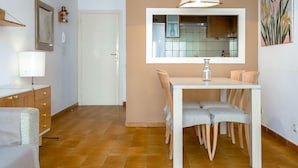 Un comedor con una mesa, sillas, una lámpara colgante y una cocina visible a través de una partición de vidrio.