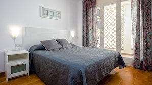 Un dormitorio con cama, mesitas de noche, una lámpara de pared y cortinas en la ventana.
