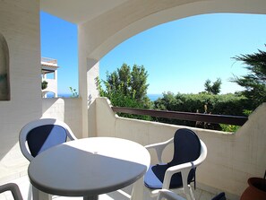 A balcony with a white table and two chairs, overlooking a scenic view with trees and a building in the distance.