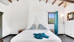 A bedroom with a bed under a canopy, a window with curtains, a floor lamp, and a wall with a geometric painting. - Villa Kromboon with a private pool, spectacular views and jacuzzi (Kralendijk)