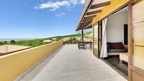 A balcony with a view of the sea, a dining area with chairs and a table, and a room with a sofa and curtains. - Villa Kromboon with a private pool, spectacular views and jacuzzi (Kralendijk)