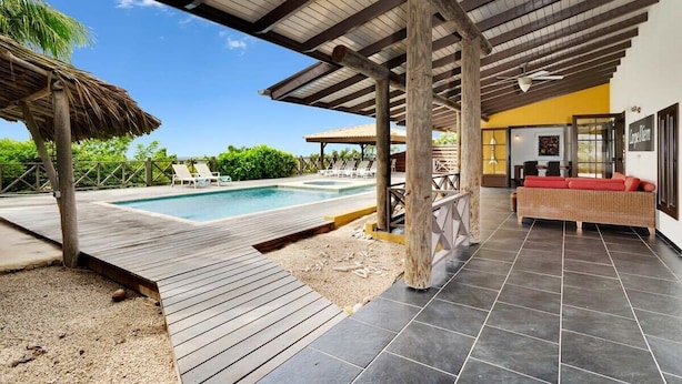 A covered outdoor area with a pool, wooden deck, and a seating area with a sofa. - Villa Kromboon with a private pool, spectacular views and jacuzzi (Kralendijk)