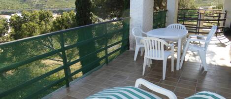 A balcony with a table and chairs, a striped lounge chair, and a view of a green landscape.