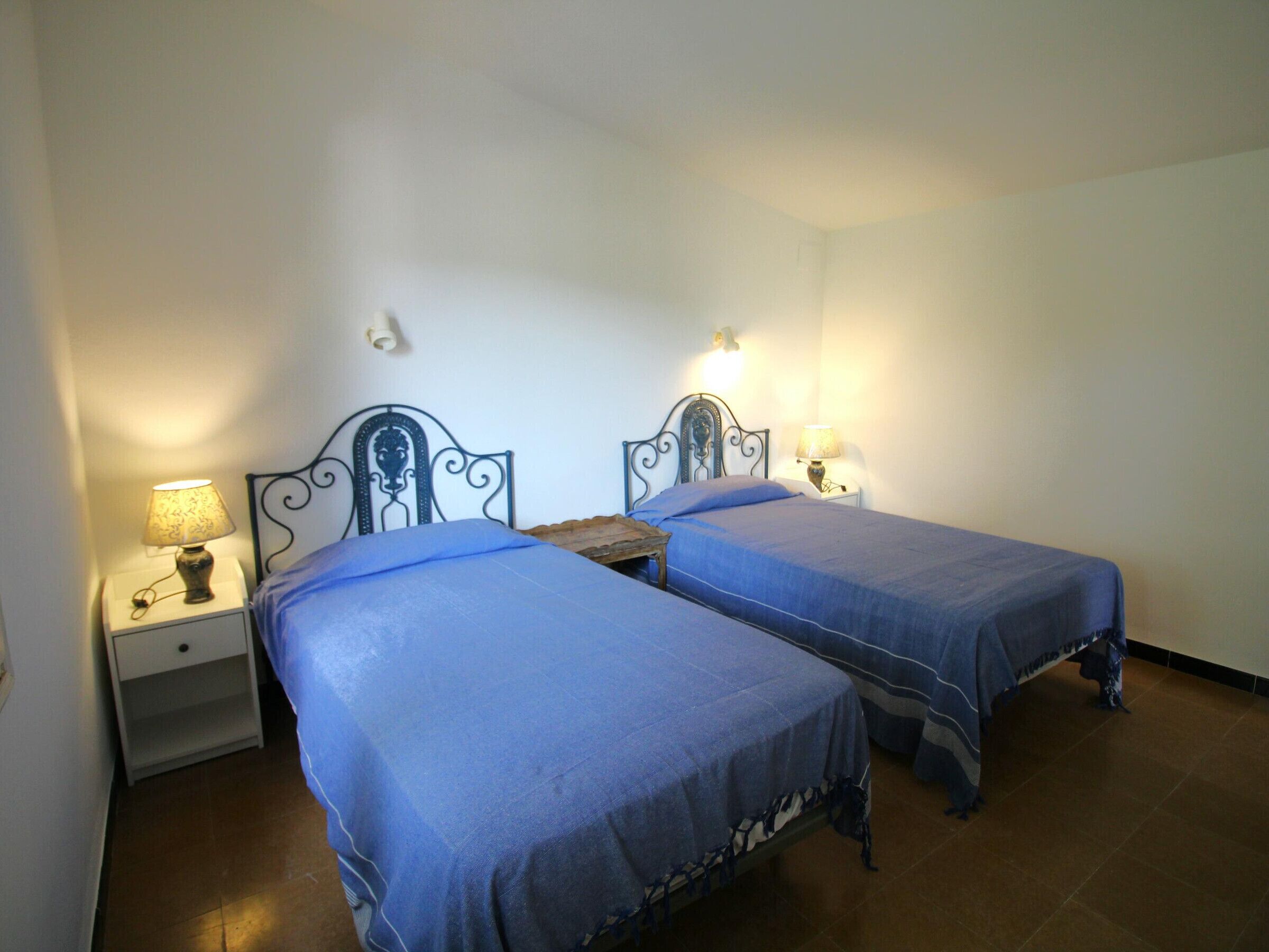 A room with two beds, each with a headboard and bedside table, and a wall-mounted light fixture.