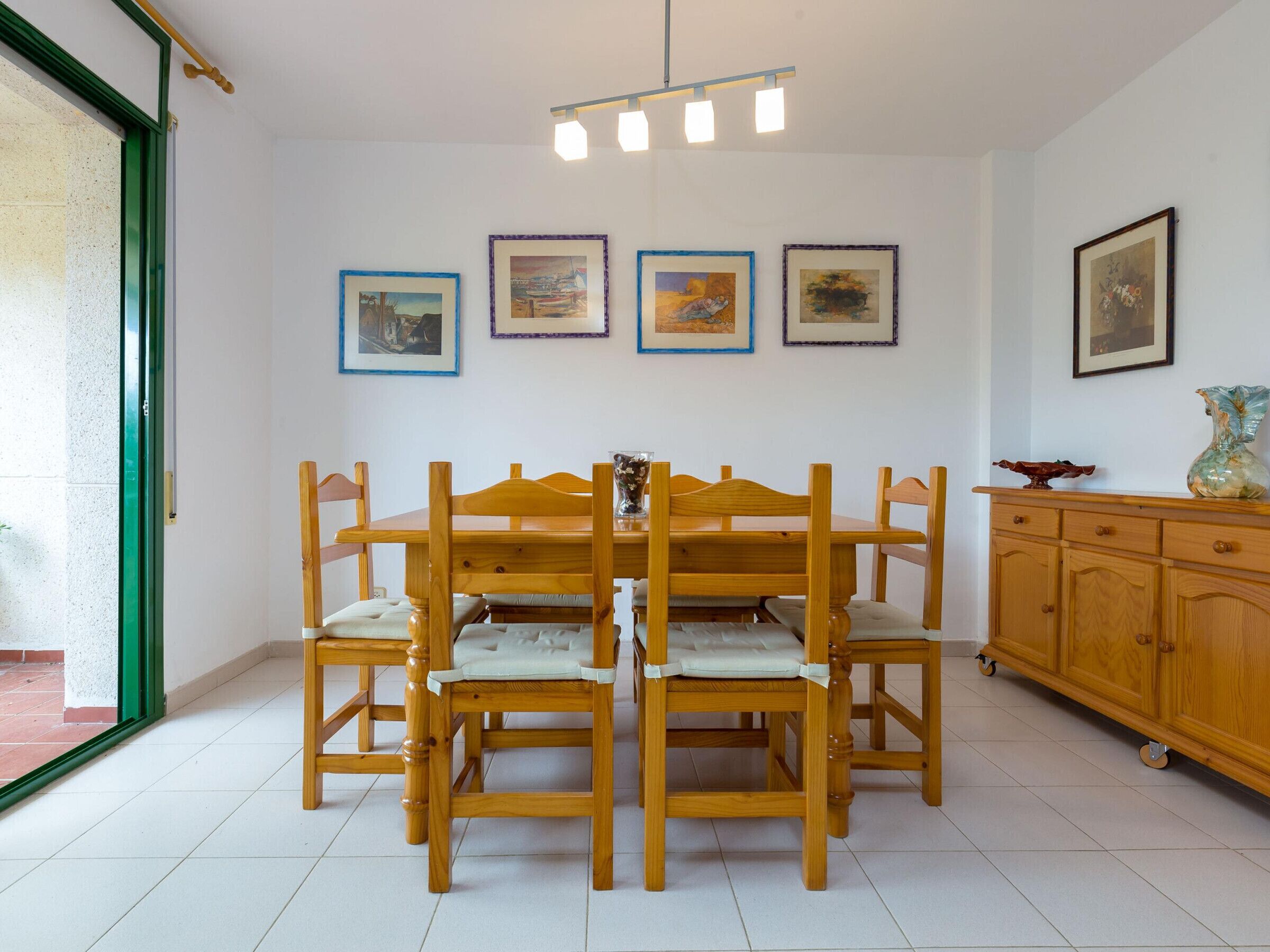 A dining area with a wooden table and chairs, a cabinet with decorative items, and framed pictures on the wall.