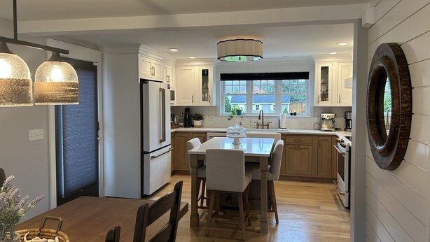 A modern kitchen with white cabinets, a central island, and a dining area with a wooden table and chairs. - Beach house, inground pool, hot tub, Large backyard,1.5 Miles from Misquamicut (Westerly)