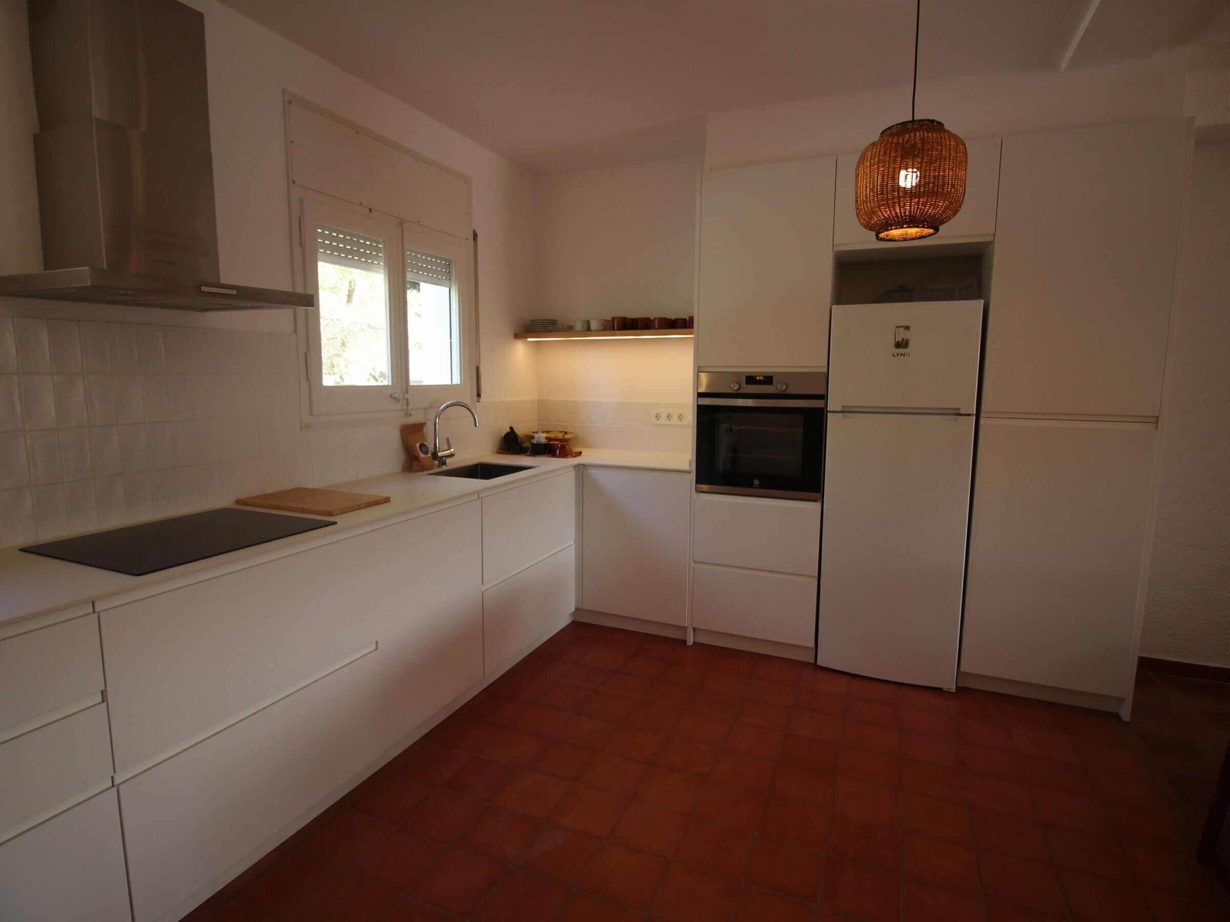 A compact kitchen with white cabinetry, a built-in oven, a refrigerator, and a hanging light fixture.