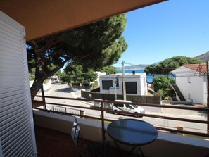 Un balcon donnant sur une zone côtière, avec un bâtiment blanc et une voiture garée.