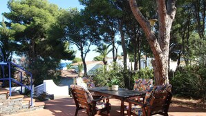 An outdoor patio with a wooden table and chairs, surrounded by trees and a view of buildings in the background. - Spacious Apartment with Large Terrace and Garage in Fané de Baix, 50m from Llançà Bypass (Llançà)