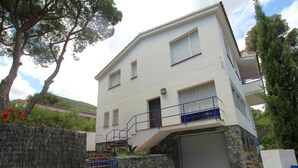 A two-story building with a stone base, a garage, and a blue railing on the upper floor. - Spacious Apartment with Large Terrace and Garage in Fané de Baix, 50m from Llançà Bypass (Llançà)