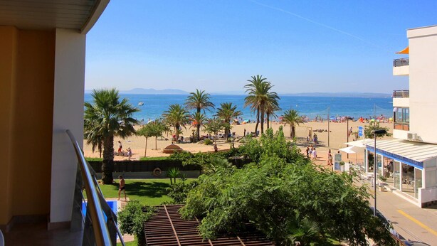 Ein Balkon mit Blick auf einen Strand, Palmen und einen klaren, blauen Himmel.