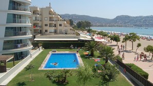 Ein Hotel mit Schwimmbad, umgeben von einer gepflegten Rasenfläche und Palmen. Es bietet mehrere Balkone und blickt auf den Strand und das Meer.