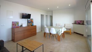 Uma sala de estar moderna com um armário de madeira, uma televisão e uma área de jantar com cadeiras brancas e uma mesa.
