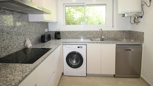 Cozinha compacta com bancadas de granito, máquina de lavar embutida, lava-louças e janela com vista para o verde.