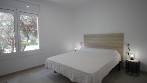 Quarto com cama grande, duas luminárias de cabeceira, uma mesa redonda pequena e uma janela com vista para árvores.