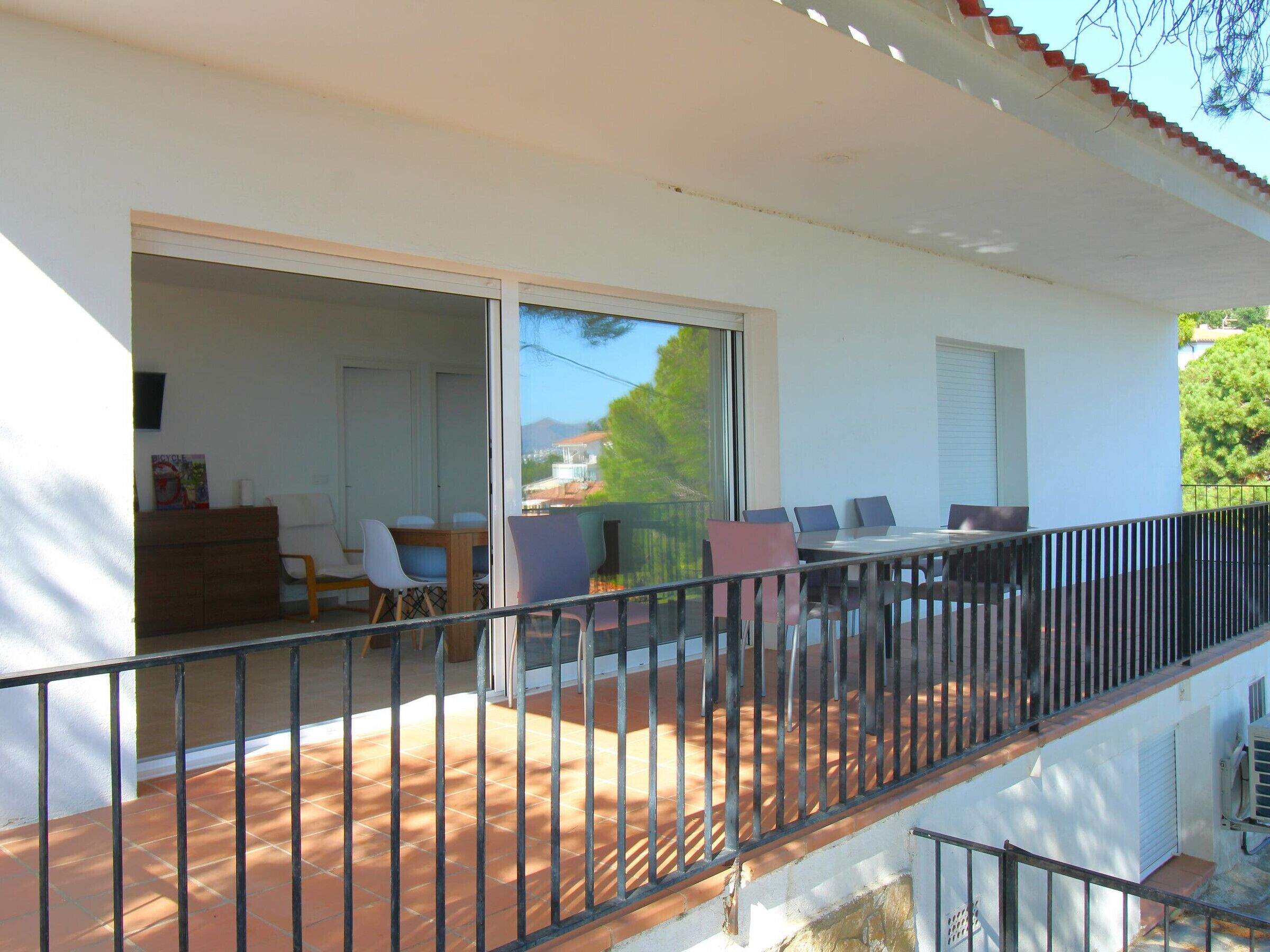Un balcon doté d’une rambarde en métal, un coin repas avec une table et des chaises, et une porte-fenêtre coulissante donnant sur un espace intérieur.