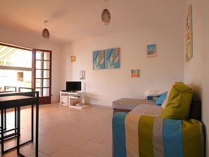 A room with a bed, a TV on a stand, a dining table, and a chair.