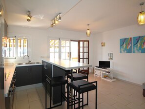 A modern kitchen with a large island, bar stools, a TV, and artwork on the walls.