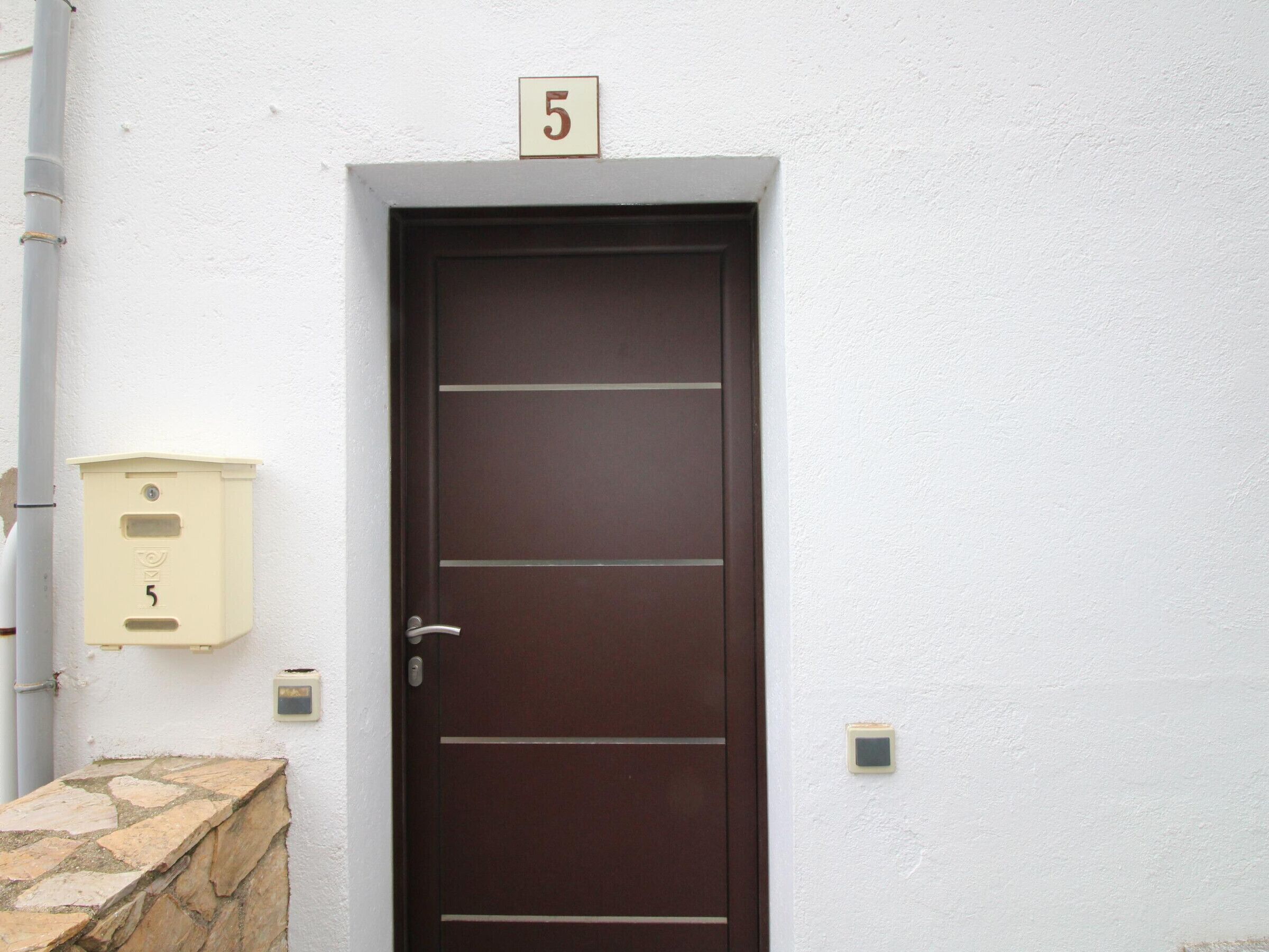 A brown door with a number 5 sign above it, a mailbox, and a stone ledge.