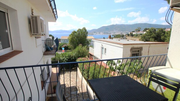 A balcony with a table and chairs, overlooking a scenic view of the sea and mountains. - 2-BR Apartment with Terrace, Sea View & Parking - Sleeps 6 (Llançà)