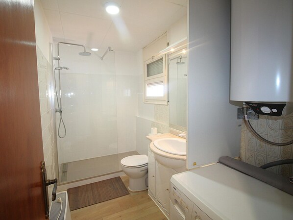 A compact bathroom with a shower, toilet, and a built-in washing machine.