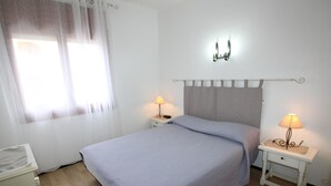 A neatly arranged bedroom with a bed, two bedside tables with lamps, a radiator, and a window with curtains. - 2-BR Apartment with Terrace, Sea View & Parking - Sleeps 6 (Llançà)