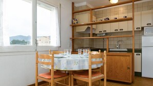 A compact kitchen with a dining table set for four, wooden chairs, a window with a view, and a built-in shelf with kitchenware.