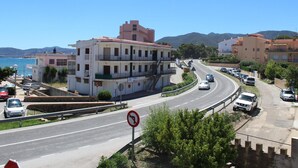 A coastal road with a multi-story building, parked cars, and a clear blue sky.