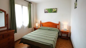 A bedroom with a wooden bed, two bedside tables with lamps, a dresser, and a window with green curtains.