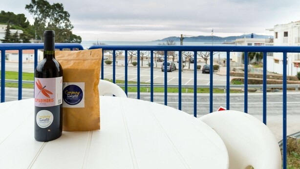 A bottle of wine and a brown paper bag on a white table with a blue railing in the background.