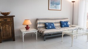 A living room with a sofa, a small table with a lamp, a cabinet, and a framed picture on the wall. - Bright apartment with pool and terrace, near the beach (Llançà)
