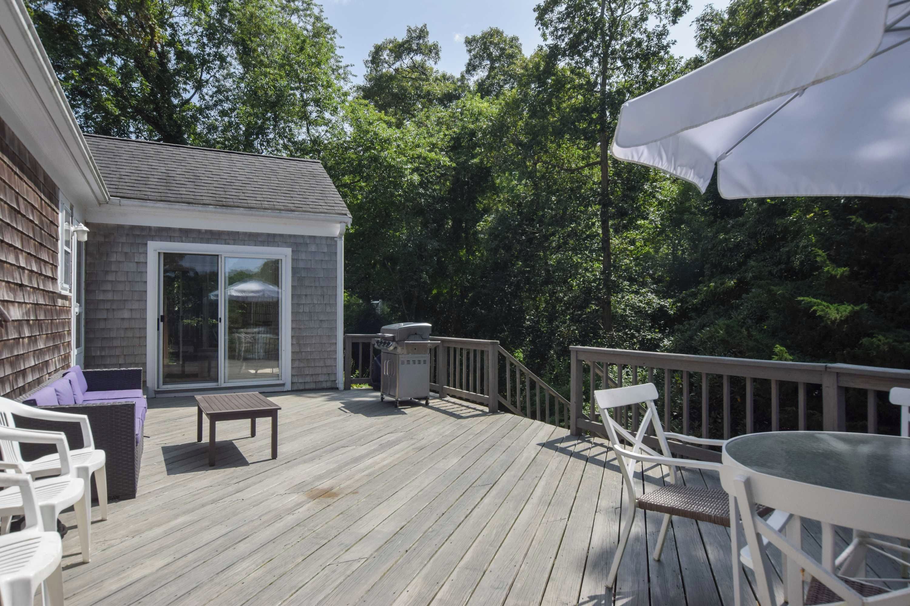 A wooden deck with outdoor furniture, a small building with a glass door, and a white umbrella.