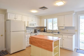 A kitchen with white cabinets, a microwave, a stove, and a wooden island.