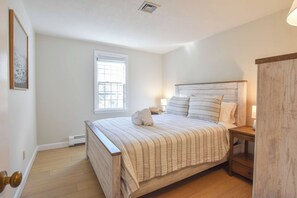 A bedroom with a bed, bedside tables, a window, and a door.