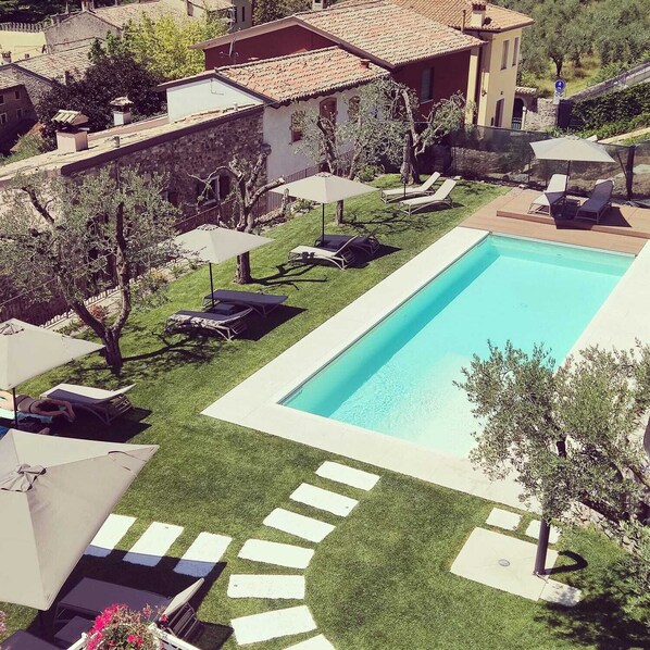 Relax by the pool surrounded by a lush garden with lounge chairs and umbrellas.