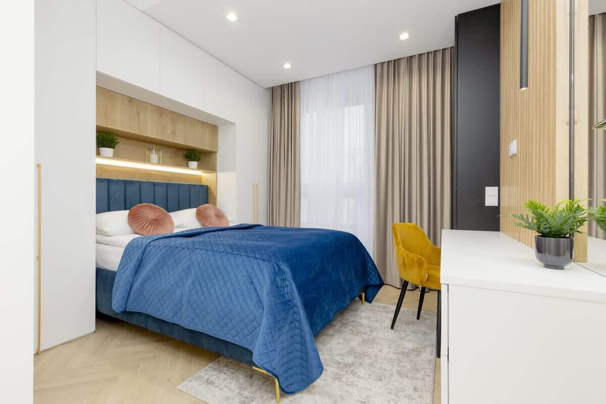A modern bedroom with a bed, bedside table, chair, and a potted plant.