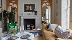 Un salon avec une cheminée, un fauteuil vert et un canapé agrémenté de coussins blancs et bleus.