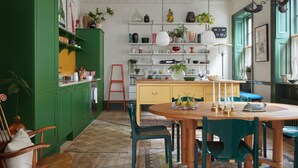 Une cuisine avec des meubles de rangement verts, une table à manger en bois et un îlot de couleur jaune.