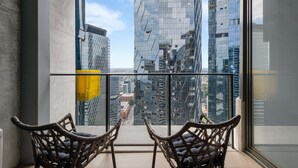 A balcony with two wicker chairs facing a cityscape of modern buildings.